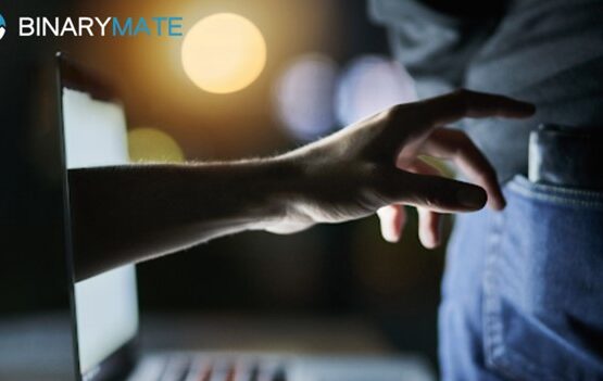 Close-up of a person's hand reaching out towards a brightly illuminated laptop screen in a dark room.