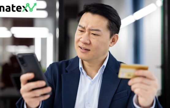 Concerned businessman holding a credit card and looking skeptically at a smartphone in an office environment.